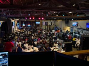 A crowded venue of people eating dinner and watching a comedian